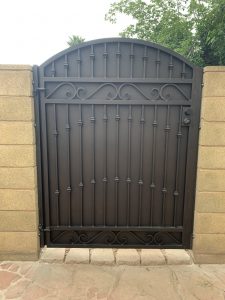 A solid, custom wrought iron gate with a decorative pattern secures the entrance to a home's yard.