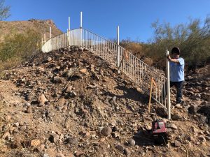 Workers install a wrought iron fence on steep terrain.